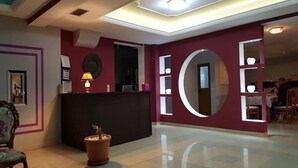 A reception area with a dark reception desk, a potted plant, and a large circular mirror on the wall. - La Perla (Sarandë)