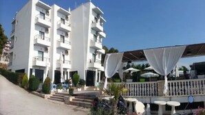 A white multi-story hotel with balconies, a covered outdoor seating area, and a staircase leading to the entrance. - La Perla (Sarandë)