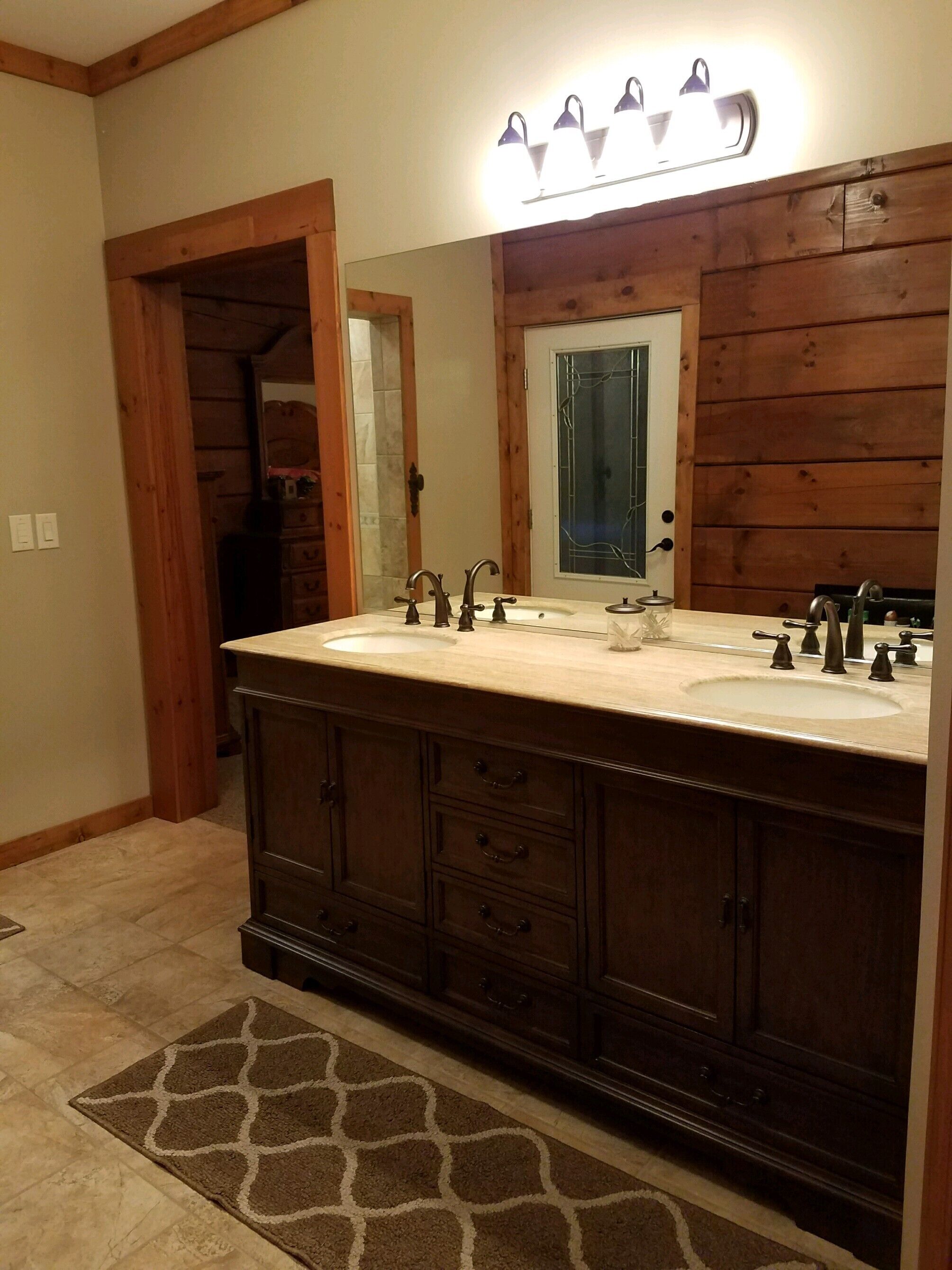 A bathroom with a double vanity, wooden cabinetry, a large mirror, and a light fixture above the mirror.