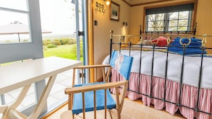 A bedroom with a bed, a chair, a table, and a window with a view of greenery.