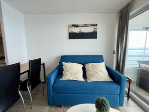 Un salon moderne avec un canapé bleu, deux coussins blancs, une petite plante en pot et un tableau accroché au mur.