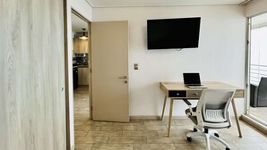 Et moderne, minimalistisk værelse med trægulv, et skrivebord med en bærbar computer, en stol og et fladskærms-tv monteret på væggen.