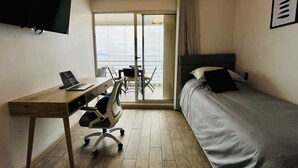 Et hotelværelse med en seng, et skrivebord med en bærbar computer, en stol og et fjernsyn ophængt på væggen.