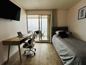 Ein Hotelzimmer mit einem Bett, einem Schreibtisch mit Laptop, einem Sessel und einem an der Wand befestigten Fernseher.
