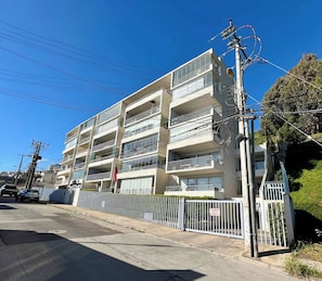 Un edificio residencial de varios pisos con balcones, entrada protegida y postes de electricidad visibles.
