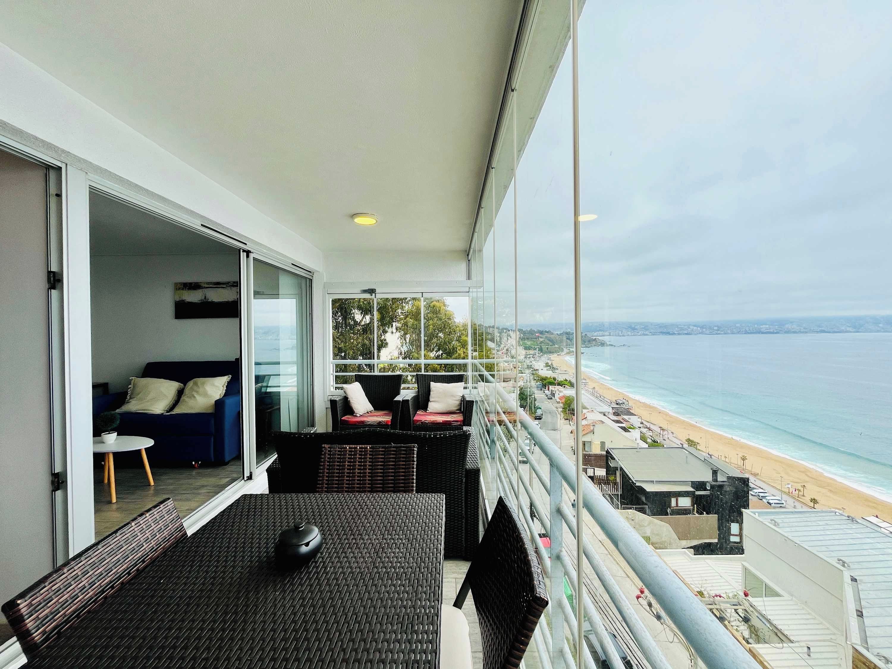 A balcony with a view of the beach, a sofa, and a dining table.
