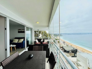 Un balcón con vistas a la playa, un sofá y una mesa de comedor.