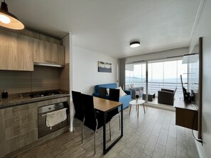 Una cocina moderna con comedor, un sofá azul y vista al mar a través de amplios ventanales.