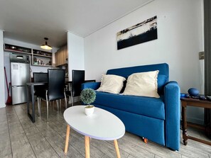 Ein Wohnzimmer mit einem blauen Sofa, einem weißen Couchtisch und einer kleinen Topfpflanze.