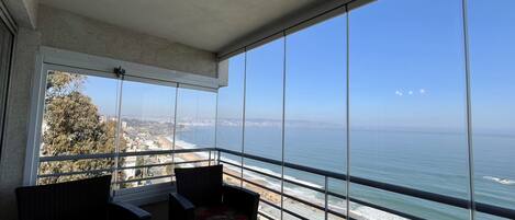 A balcony with a clear view of the ocean and a distant cityscape.