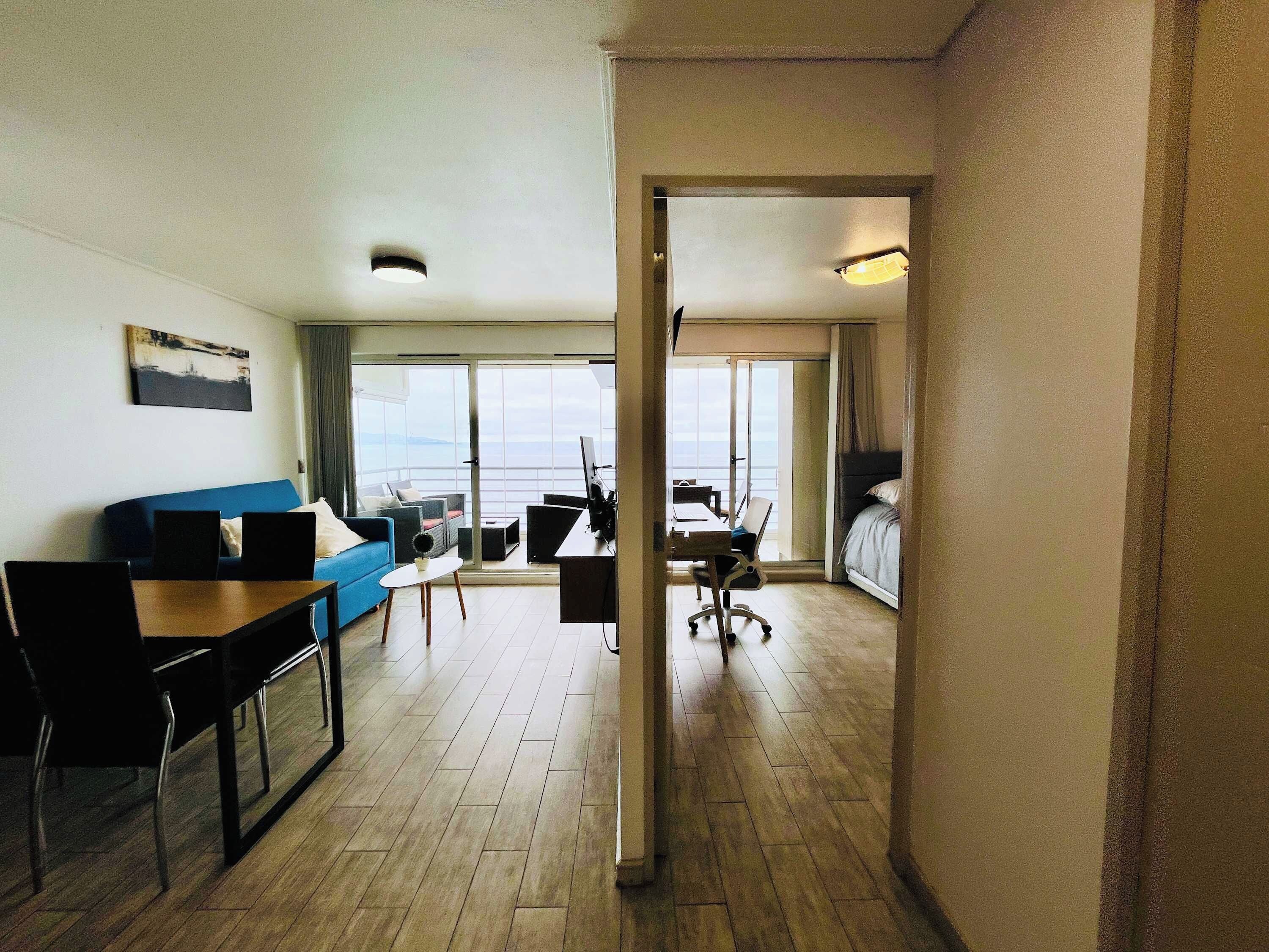 A hotel room with a balcony, a desk, a sofa, and a bed.