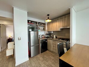 Cocina compacta con refrigerador, microondas, estufa y lavaplatos. Hay un comedor con una mesa y sillas.