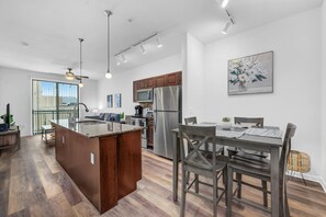 A modern kitchen with a central island, stainless steel appliances, and a dining area with a wooden table and chairs. - Magic Haven @ The Domain - ATX (Austin)