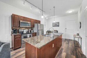 A modern kitchen with wooden cabinets, stainless steel appliances, and a granite countertop island. - Magic Haven @ The Domain - ATX (Austin)