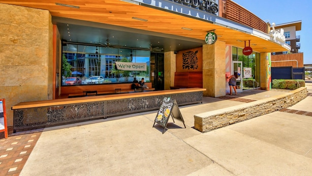 Una tienda Starbucks con fachada de madera, asientos al aire libre y un letrero que indica que está abierta.