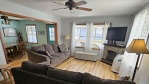 A living room with a dark grey sofa, a fireplace, a television, and a ceiling fan. - 645 Sycamore in Lakeside (Lakeside)