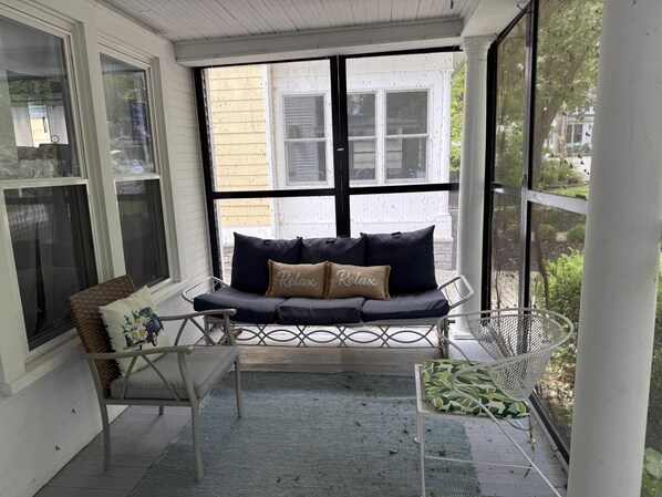 A covered porch with a cushioned bench, a wicker chair, and a metal table.