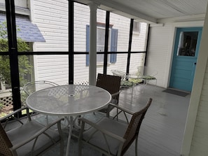 A covered patio with a round table and chairs, a blue door, and white siding.