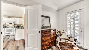 A room with a wooden dresser, a cowhide chair, and a door leading to a kitchen with white cabinets and a microwave. - Charming Casita in Cave Creek (Cave Creek)