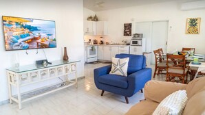 Una sala de estar moderna con televisor, un sillón azul, una mesa de centro de vidrio y un sofá color beige.
