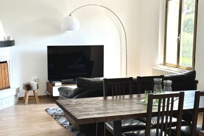 A modern living room with a flat-screen TV, a dining table, and a sofa.