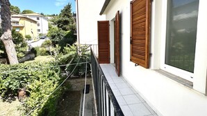 A balcony with a metal railing, wooden shutters, and a white building with a window. - S342 - Sirolo, comfortable three-room apartment near the center (Sirolo)