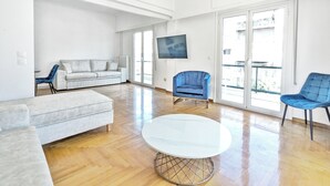 Un salón amplio con un sofá blanco, una mesa redonda de centro y dos sillones azules.