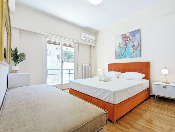 Habitación de hotel con una cama grande, una cama más pequeña, un balcón con vistas y un cuadro en la pared.