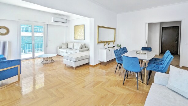 Un salón amplio con un sofá blanco, sillas azules y una mesa de comedor.