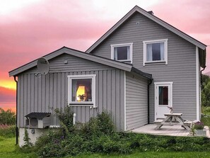 Ein zweistöckiges Haus mit Satellitenschüssel, einer kleinen Veranda mit Tisch und einem Garten.
