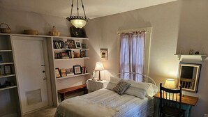 A cozy bedroom with a bed, bedside tables, a chair, a wardrobe, and shelves with personal items. -  Sunday Haus- 2 blocks from Main Street! Sleeps 4 (Fredericksburg)