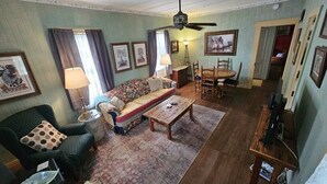 A living room with a sofa, armchairs, a coffee table, and a dining table with chairs. There is a ceiling fan, a lamp, and framed pictures on the walls. -  Sunday Haus- 2 blocks from Main Street! Sleeps 4 (Fredericksburg)