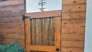 Una verja de madera con paneles verticales de bambú, un picaporte negro y una base de hormigón.