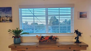 Un comedor con una mesa de madera, dos sillas acolchadas, un ventanal decorativo con persianas, una planta en maceta y un letrero en la pared que dice "Blessed At The Beach".