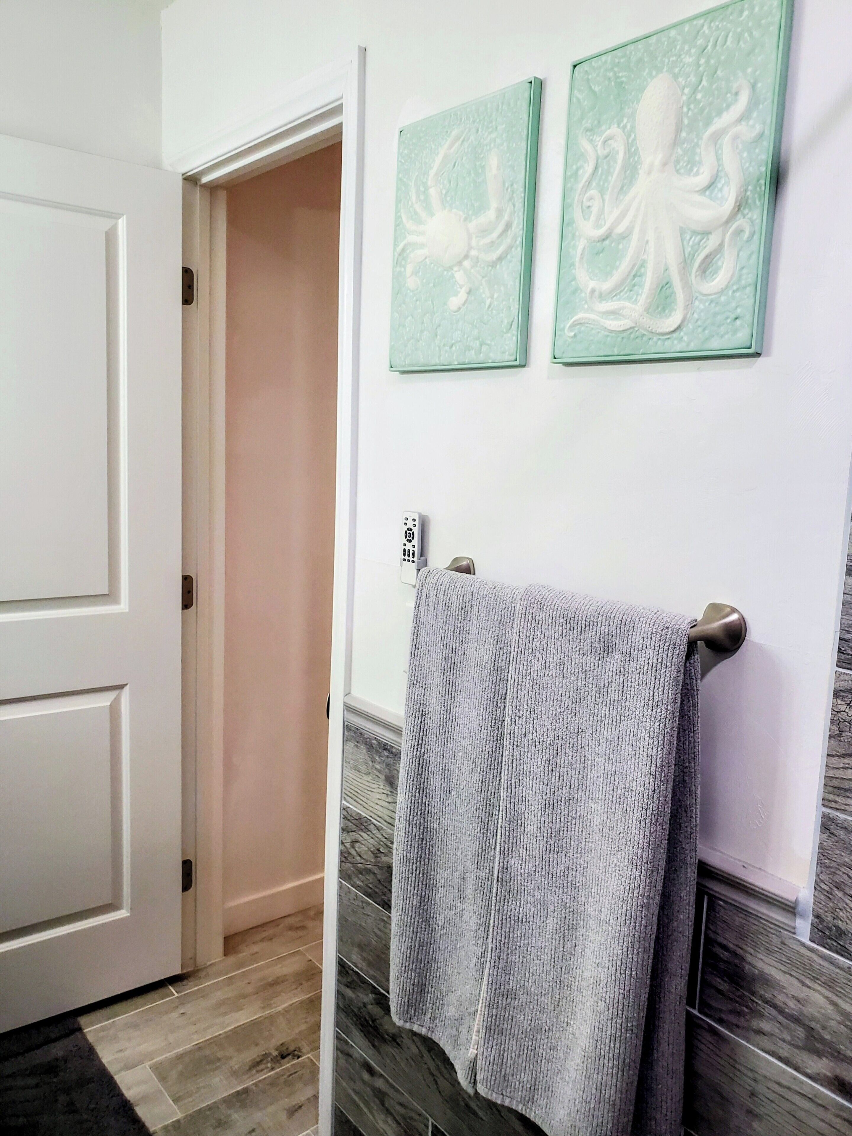 A bathroom with a towel rack, a door, and two framed wall art pieces.