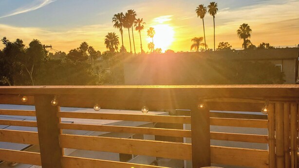 Vista del atardecer desde un balcón con una bebida y luces colgantes.