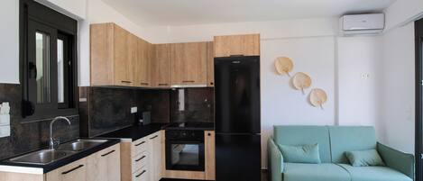Una cocina moderna con armarios de madera, un refrigerador negro y un sofá color turquesa.