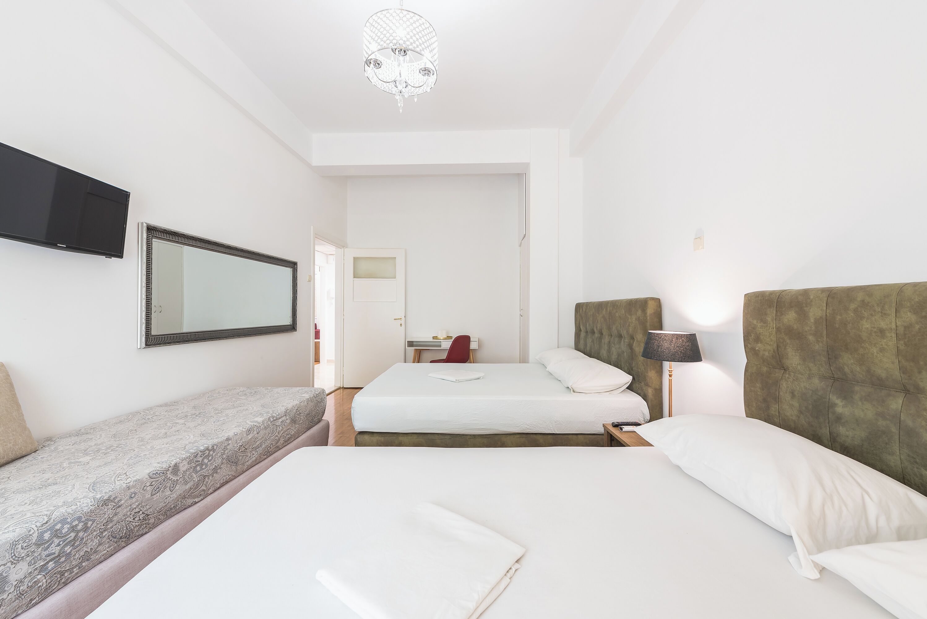 A hotel room with two beds, a TV, a mirror, a chandelier, and a door leading to a bathroom.