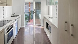 A modern kitchen with stainless steel appliances, a sliding glass door leading to a patio, and a clean, tiled floor. - H2O Holiday Apartments - Unit 10 (North Haven)