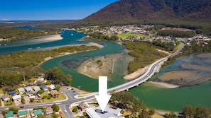 An aerial view of a coastal town with a prominent bridge connecting two areas, surrounded by lush greenery and a river.