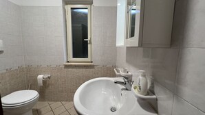 Une salle de bain avec des toilettes, un lavabo et une fenêtre située au-dessus du lavabo.
