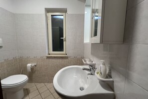 Une salle de bain avec des toilettes, un lavabo et une fenêtre située au-dessus du lavabo.