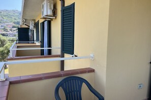 Un balcon avec une chaise, une balustrade et une fenêtre avec des volets.