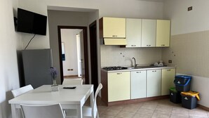 Une cuisine compacte avec un coin repas, un téléviseur fixé au-dessus du réfrigérateur et un pare-feu en carreaux.