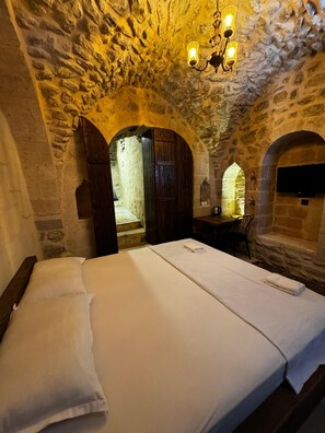 Una habitación de paredes de piedra con una cama, una puerta de madera y un candelabro.