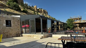 A restaurant with outdoor seating, stone walls, and a view of a rocky hillside. - Kochan Konagi (Mardin)