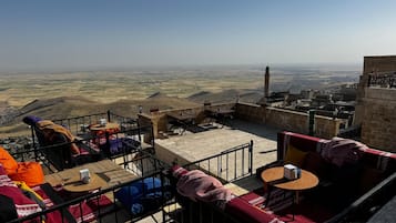 Una terraza en la azotea con mesas al aire libre, vistas del paisaje y una torre a lo lejos.