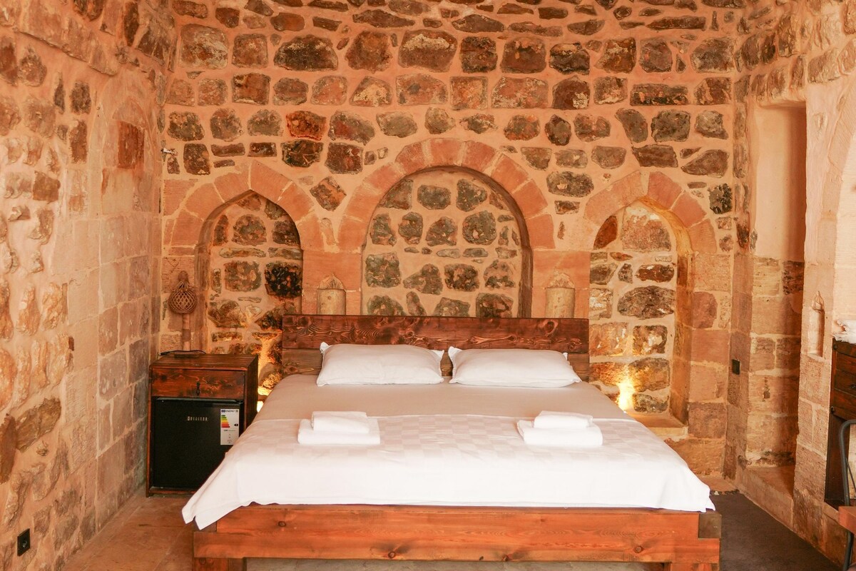 Una habitación de paredes de piedra con una cama, una mesita de noche y un cabecero de madera.