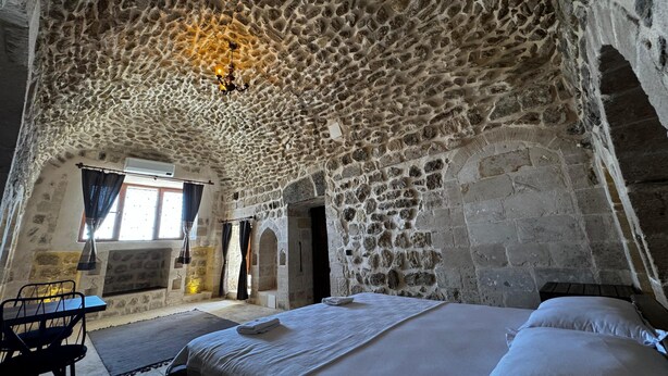 A stone-walled room with a bed, a table, and a window. - Kochan Konagi (Mardin)