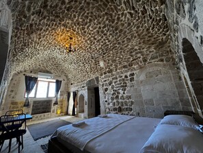 A stone-walled room with a bed, a table, and a window. - Kochan Konagi (Mardin)